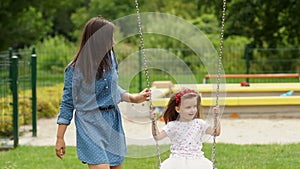 Happy Family Spending Time Together During Summer Warm Day on the Playground. Little Girl Riding a Swing Outdoors.