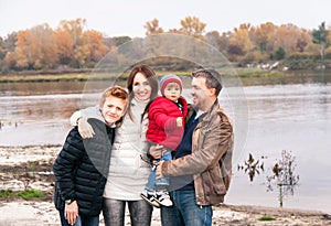 Happy family is standing near the river in the autumn day.