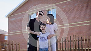 Happy family standing near their house in sunny summer day embracing each other. Father, mother and son feeling glad