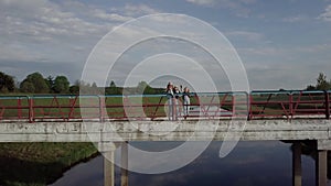A happy family is standing on the old bridge and waving hands.