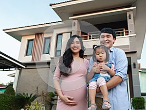 Happy family standing outside house, husband and pregnant wife and baby girl
