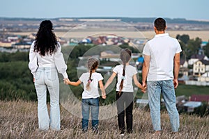 Happy family stands joining hands with children on hill top