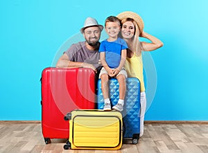 Happy family with suitcases near color wall.