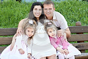 Happy family in summer city park outdoor, pregnant woman, parent and children, bright sunny day and green grass, beautiful people