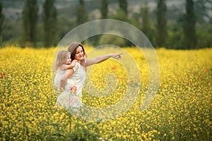 Happy family summer vacation. Mother with girl in rape field enjoying life at sunset. Pretty brunette with long healthy