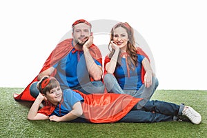happy family of superheroes sitting on lawn and smiling at camera