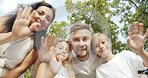 Happy family taking selfie or recording video leaning over the camera smiling and waving during summer vacation