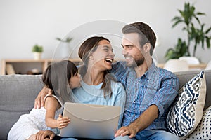 Happy family of three bonding using laptop sitting on couch