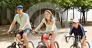 Happy family of three cycling on street