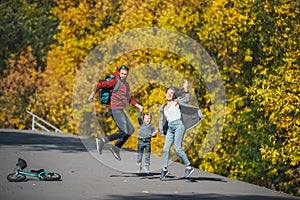 Happy family of three jumping on rural road in solar autumn day