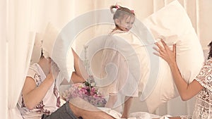 Happy family of three: mother, father and daughter having a pillow fight in bed