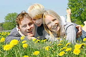 Happy Family of Three People Relaxing in Flower Meadow