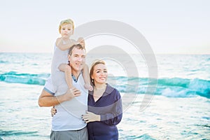 Happy family of three - pregnant mother, father and daughter embracing, laughhing and having fun walking on the beach. Family vaca