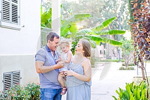 Happy family of three - pregnant mother, father and daughter hugging, laughing, having fun in the sunset park. Family recreation,