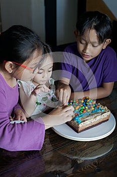 Happy family with three sibling decorating birthday cake at home.