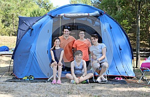 Happy family with three smiling children and tent in summer camp