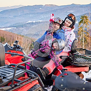 Happy family of three spending great time together in the mountains in winter riding quad bike