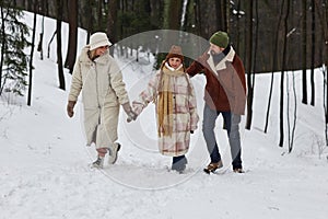 Happy family of three in winterwear walking along forest road covered with snow
