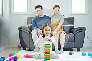 Happy Family Time of asian parent looking at their daughter smiling playing with toy build wooden blocks board game in moments