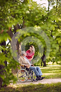 happy family time- elderly man in wheelchair talking with daughter in the park.