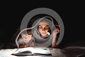 Happy family. Time for stories. Delighted happy cute mother and son enjoying a book before sleeping and using a flashlight