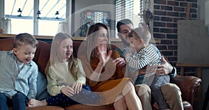 Happy family time together, young Caucasian mother, father and three kids sit together to watch TV at home slow motion.