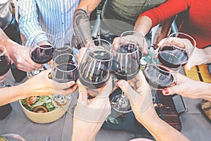 Happy family toasting with red wine glasses at dinner outdoor - People having fun cheering and drinking while dining together