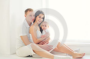 Happy family together, mother and father with little baby home in white room near window