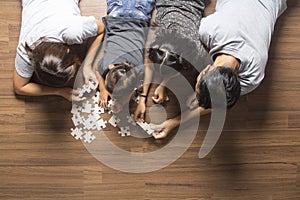 Happy family top view lying on floor with jigsaw puzzle