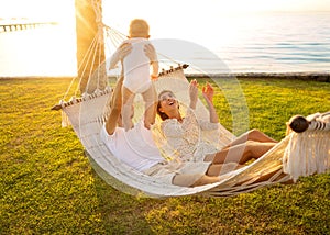 Happy family on a tropical island at sunset lie in a hammock and play with their son