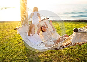 Happy family on a tropical island at sunset lie in a hammock and play with their son