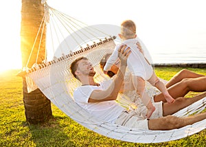 Happy family on a tropical island at sunset lie in a hammock and play with their son