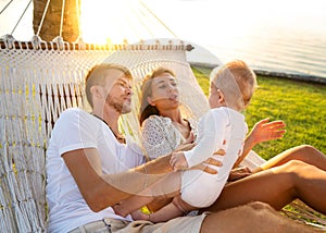 Happy family on a tropical island at sunset lie in a hammock and play with their son