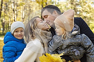 Happy family with two children in the autumn park hugging and kissing. Love, tenderness and warm relations in the family.