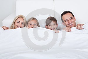 Happy Family With Two Children In Bed Under Cover