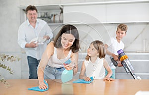 Happy family with two children doing cleaning in kitchen