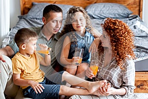 Happy family with two children drinking fresh orange juice near the bed