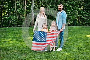 happy family with two children holding us flag and smiling at camera in park