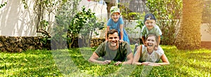 happy family with two children lying in the home backyard garden lawn and looking at camera. banner