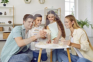 Happy family with two children are playing puzzles at table sitting on floor at home in weekend.