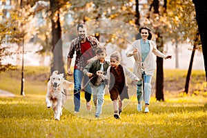 Happy family with two children running after a dog together