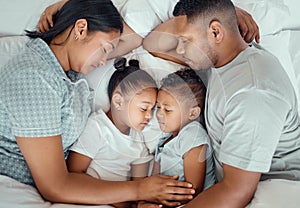 Happy family with two children sleeping together in their parents bed, from above. Loving parents cuddling two little