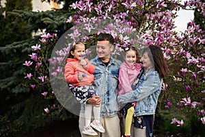 Happy family with two daughters enjoying nice spring day near magnolia blooming tree