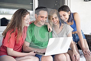 Happy Family With Two Daughters Using Laptop Together. Sitting on a Sofa at the Balcony