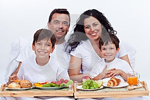 Happy family with two kids having breakfast in bed