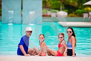 Happy family with two kids in swimming pool. Smiling parents and children on summer vacation swim and having fun.