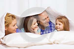 Happy family with two kids under blanket at home