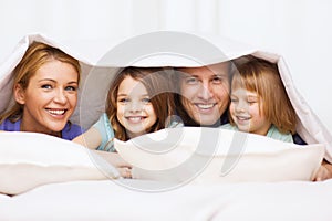 Happy family with two kids under blanket at home