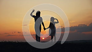 Happy family two sisters sunset walks at in the park silhouette say goodbye waving hand. two daughters. kid dream