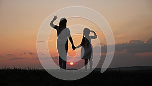 happy family two sisters sunset walks at in the park silhouette say goodbye waving hand. two daughters. kid dream